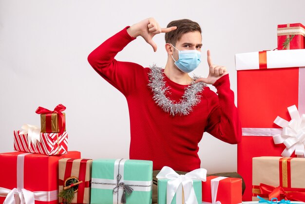 Vooraanzicht jonge man met masker camera teken rond xmas geschenken zitten