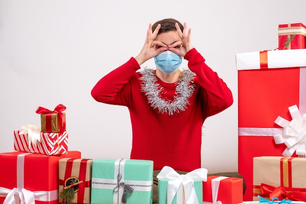 Vooraanzicht jonge man met masker verrekijker handen aan zijn ogen zitten rond xmas geschenken