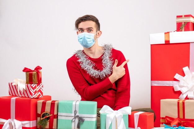 Vooraanzicht jonge man met masker wijzend op geschenken rond kerstcadeaus zitten