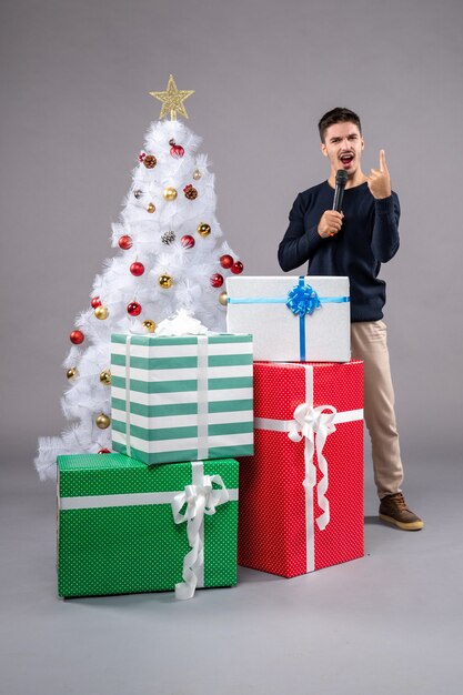 Vooraanzicht jonge man met microfoon met cadeautjes op het grijs