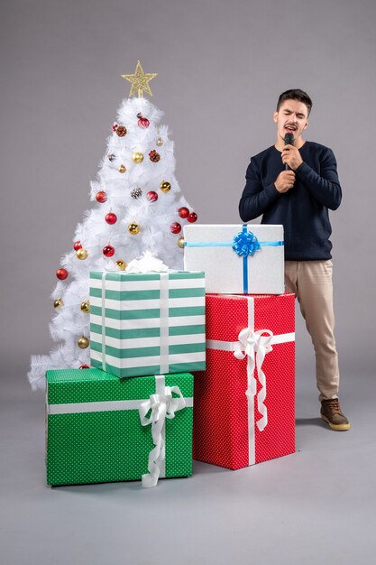Vooraanzicht jonge man met microfoon met cadeautjes op het grijs