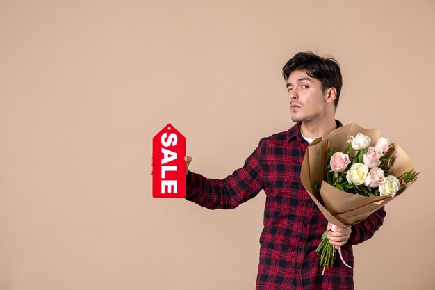 Vooraanzicht jonge man met mooie bloemen en verkoop naambordje op bruine muur