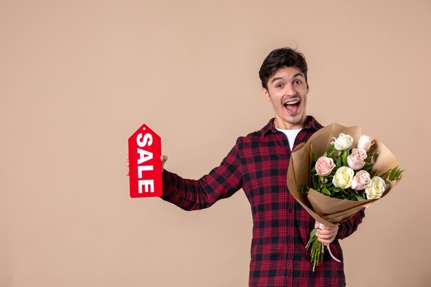 Vooraanzicht jonge man met mooie bloemen en verkoop naambordje op bruine muur