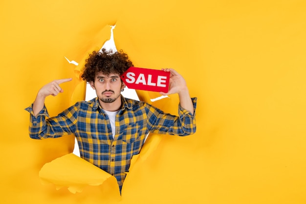 Gratis foto vooraanzicht jonge man met rode verkoop schrijven op gele gescheurde achtergrond