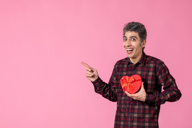 Vooraanzicht jonge man met rood hartvormig cadeau op roze muur