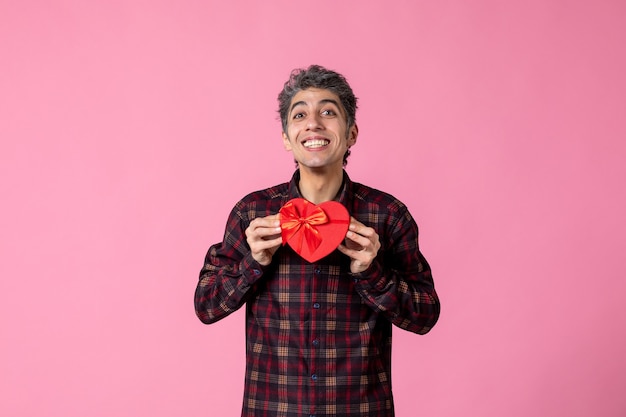 Vooraanzicht jonge man met rood hartvormig cadeau op roze muur