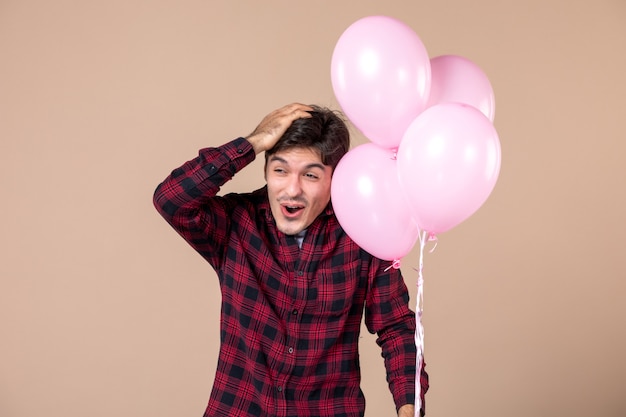 Vooraanzicht jonge man met roze ballonnen op bruine muur