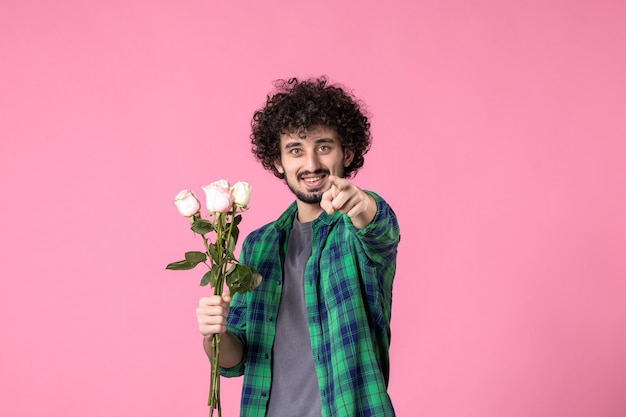 Vooraanzicht jonge man met roze rozen als cadeau voor vrouwendag op roze kleur