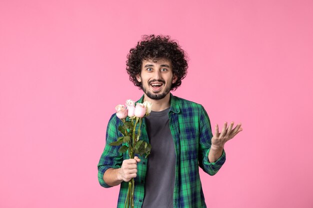 Vooraanzicht jonge man met roze rozen als cadeau voor vrouwendag op roze kleur