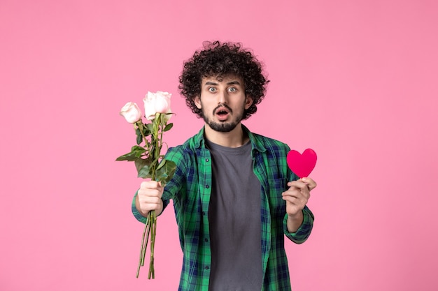 Vooraanzicht jonge man met roze rozen en hartsticker op roze