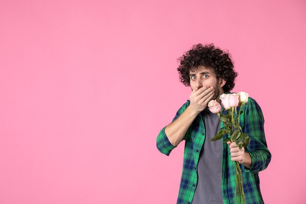 Vooraanzicht jonge man met roze rozen op roze