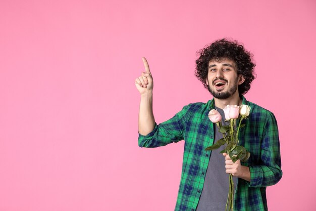 Vooraanzicht jonge man met roze rozen op roze