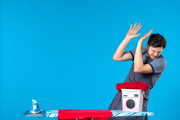 Vooraanzicht jonge man met strijkplank op blauwe achtergrond Wasserij ijzer kleur wasmachine schoonmaak man