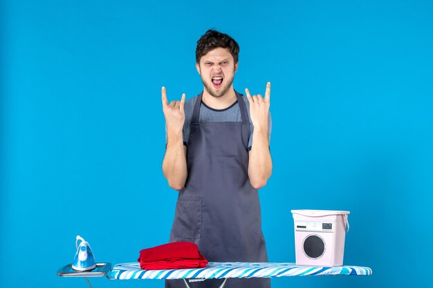 Vooraanzicht jonge man met strijkplank op de blauwe achtergrond huishoudelijk werk kleur ijzer Wasserij wasmachine man reiniging