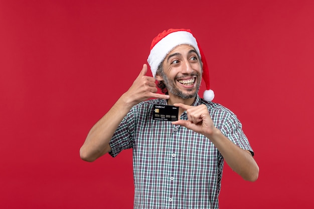 Vooraanzicht jonge man met zwarte bankkaart op de rode achtergrond