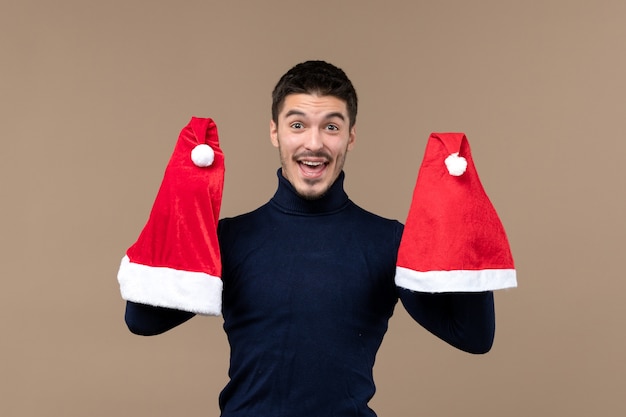 Vooraanzicht jonge man spelen met rode kappen op bruine achtergrond Kerstmis emoties Nieuwjaar