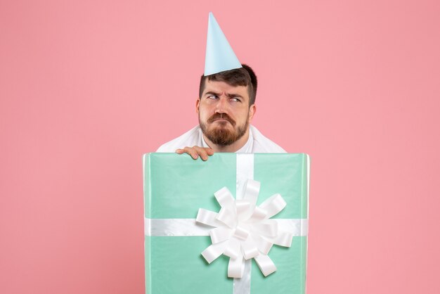 Vooraanzicht jonge man staande in huidige doos op roze bureau xmas foto kleur emotie pyjama party