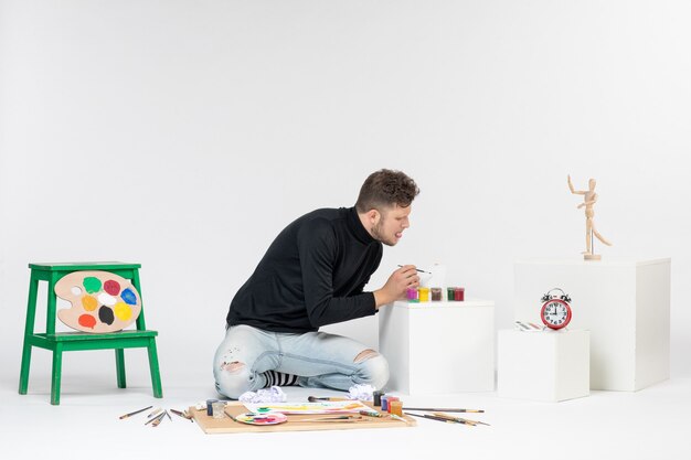 Vooraanzicht jonge man werken met verf op witte muur foto kunst foto schilderij tekenen kleur kunstenaar verf