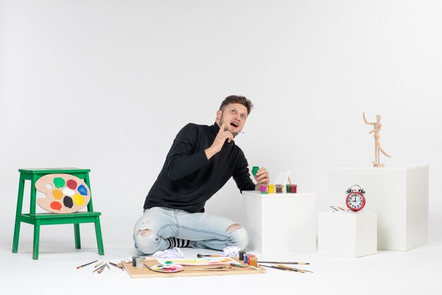 Vooraanzicht jonge man werken met verf op witte muur kunstenaar verf kunst kleur schilderij foto tekenen foto