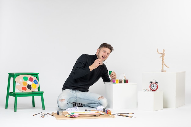 Vooraanzicht jonge man werken met verf op witte muur verf kunst kleur kunstenaar schilderijen foto foto tekenen