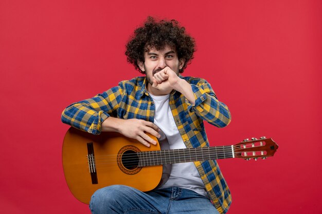 Vooraanzicht jonge man zittend met gitaar op een rode muur speel concert live muziek kleur muzikant applaus band