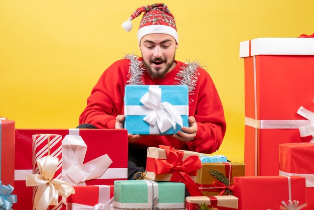 Vooraanzicht jonge man zittend rond kerstcadeautjes op gele achtergrond