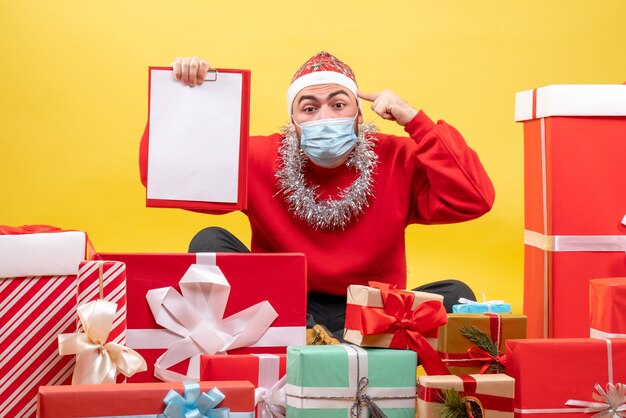 Vooraanzicht jonge man zittend rond kerstcadeautjes op gele achtergrond