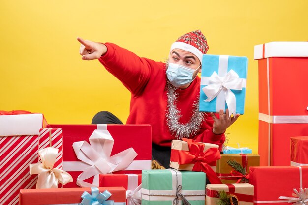 Vooraanzicht jonge man zittend rond kerstcadeautjes op gele achtergrond