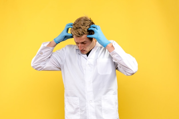 Vooraanzicht jonge mannelijke arts aarzelt op gele achtergrond menselijke covid-pandemische medic