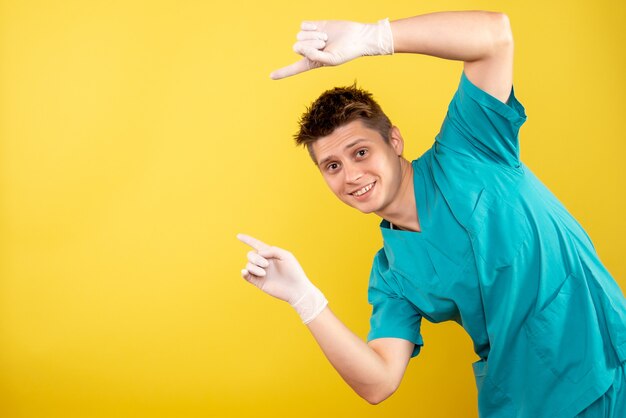 Vooraanzicht jonge mannelijke arts in medisch kostuum met handschoenen op gele achtergrond