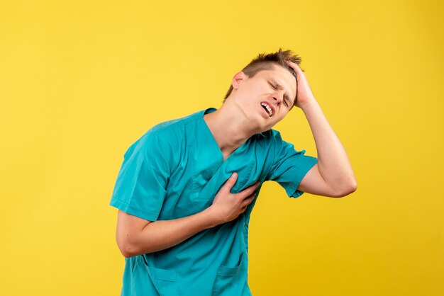 Vooraanzicht jonge mannelijke arts in medisch kostuum met hartpijn op gele achtergrond