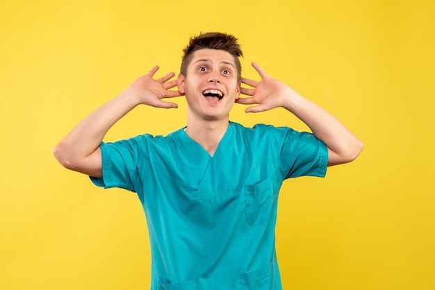 Vooraanzicht jonge mannelijke arts in medisch kostuum op de gele achtergrond