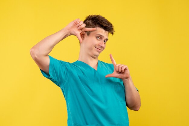 Vooraanzicht jonge mannelijke arts in medisch kostuum op de gele achtergrond