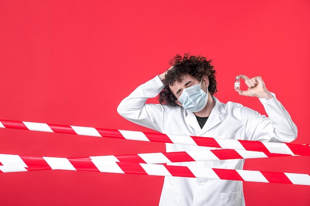 Vooraanzicht jonge mannelijke arts in medisch uniform met kolf op rode achtergrond strip gevaar ziekenhuis quarantaine covid-kleur waarschuwing gezondheid