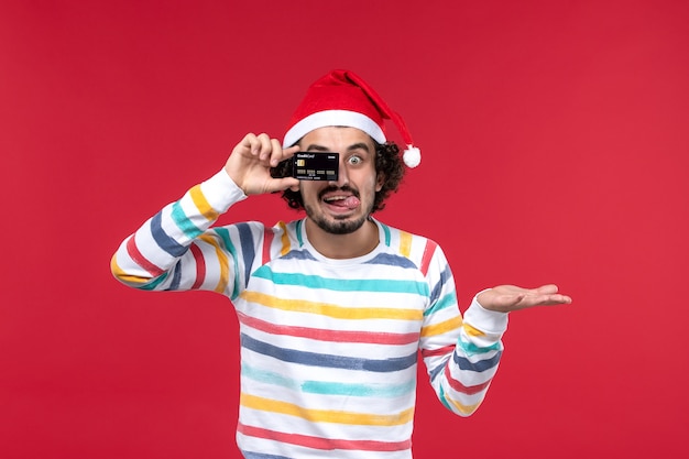 Gratis foto vooraanzicht jonge mannelijke bankkaart op rode muur mannelijke rode vakantie emotie