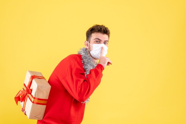 Vooraanzicht jonge mannelijke kerstcadeau achter zijn rug verbergen