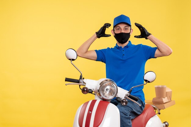 Vooraanzicht jonge mannelijke koerier in blauw uniform op de gele achtergrond werk covid-job pandemie bezorgdienst virus fiets