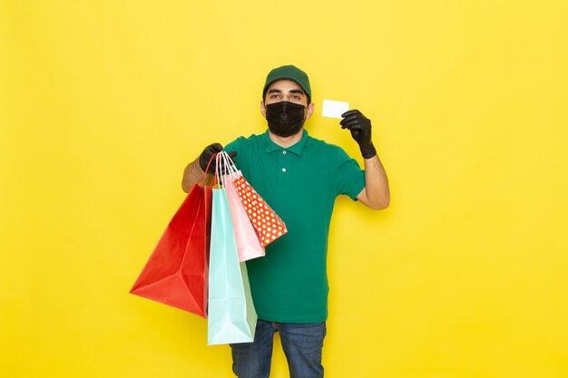 Vooraanzicht jonge mannelijke koerier in groen shirt groen pet met wit bord en winkelen pakketten op de gele achtergrond service kleur leveren