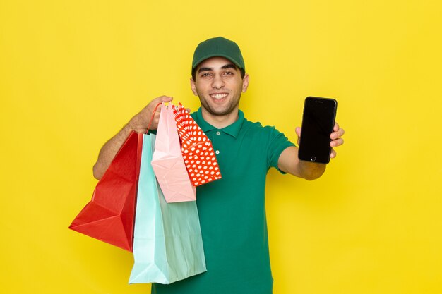 Vooraanzicht jonge mannelijke koerier in groen shirt groene pet met telefoon en winkelpakketten op geel