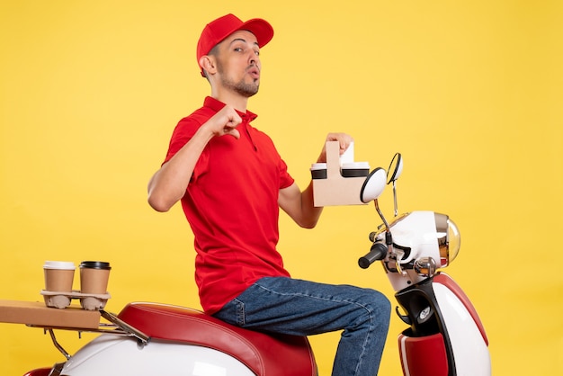 Vooraanzicht jonge mannelijke koerier in rood uniform met koffie op gele achtergrond