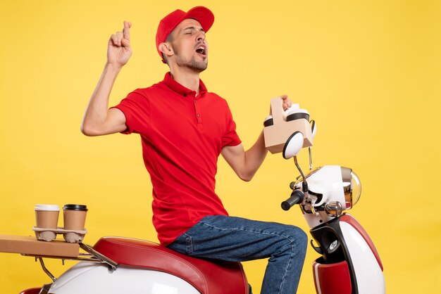 Vooraanzicht jonge mannelijke koerier in rood uniform met koffie op gele achtergrond