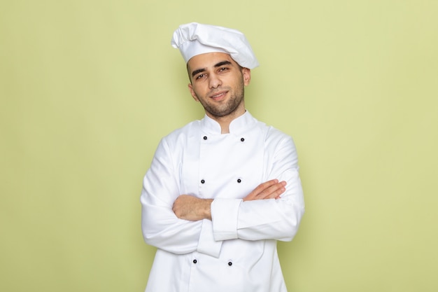 Vooraanzicht jonge mannelijke kok in witte kok pak poseren met gekruiste armen op groen