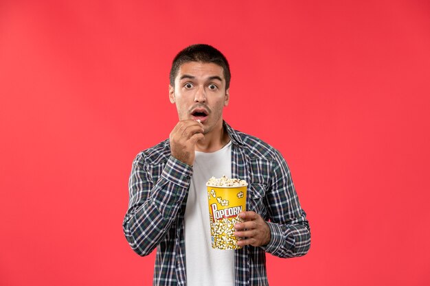 Vooraanzicht jonge mannelijke popcornpakket houden en eten op lichte rode muur bioscoop theater film mannelijke film