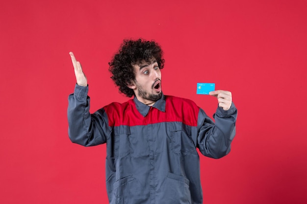 Vooraanzicht jonge mannelijke werknemer in uniform met blauwe bankkaart op rood oppervlak