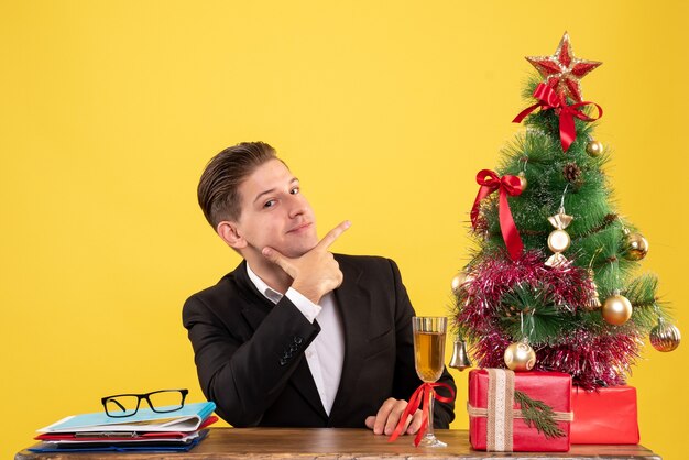 Vooraanzicht jonge mannelijke werknemer zitten met kerstcadeautjes en boom