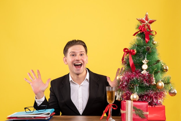 Vooraanzicht jonge mannelijke werknemer zitten met kerstcadeautjes en boom