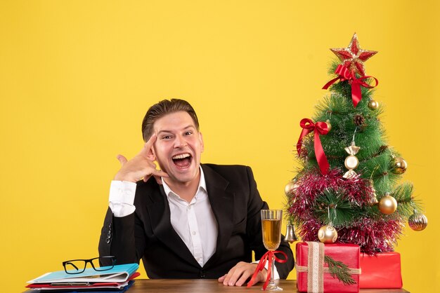 Vooraanzicht jonge mannelijke werknemer zitten met kerstcadeautjes en boom