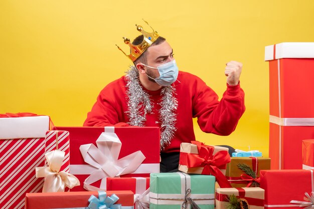 Vooraanzicht jonge mannelijke zittend rond kerstcadeautjes in masker op gele achtergrond