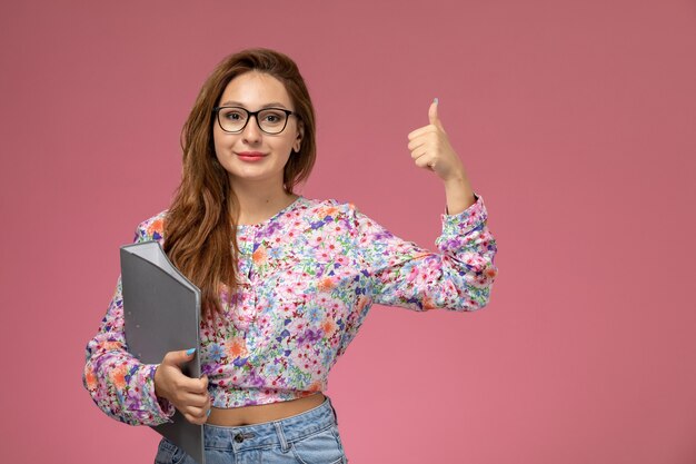 Vooraanzicht jonge mooie vrouw in bloem ontworpen shirt en spijkerbroek grijs bestand met glimlach op de roze achtergrond te houden