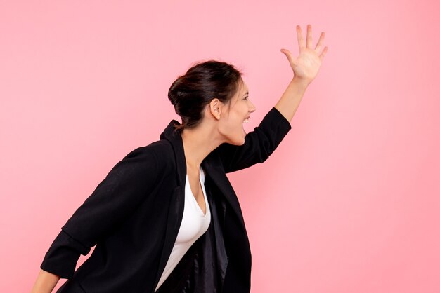 Vooraanzicht jonge mooie vrouw in een donkere jas op de roze achtergrond